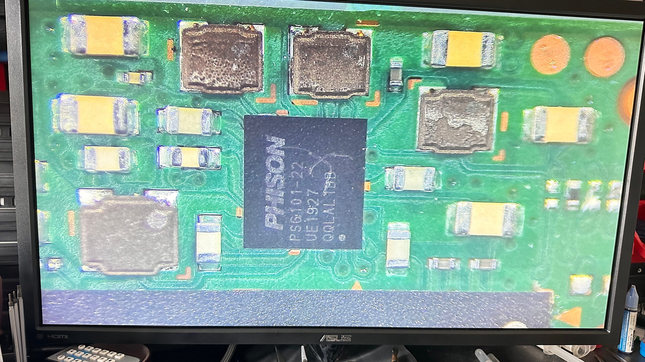PHISON PS6101-22 uszkodzony kontroler zasilania - Power Management IC wraz ze spalonymi cewkami Na zdjęciu widoczny jest zbliżony widok na układ scalony na płytce drukowanej, z dużym napisem Phison. To element prawdopodobnie związany z kontrolerem pamięci masowej, stosowanym w dyskach SSD. Otaczają go różne elementy elektroniczne, takie jak kondensatory i rezystory. Taki obraz może być częścią diagnostyki układów elektronicznych w procesie analizy i naprawy pamięci masowych.